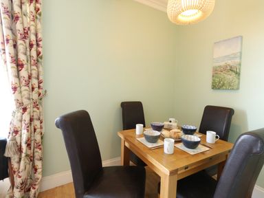 A dining room with a wooden table set for four with bowls and mugs and brown chairs at Tradewinds Brewers Quay Harbour