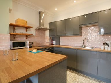 A kitchen with wooden countertops gray cabinets pink tiled backsplash a microwave oven and a sink at Tradewinds Brewers Quay Harbour