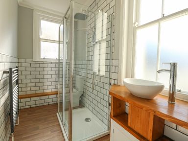 A bathroom with a glass shower enclosure a white sink on a wooden countertop and tiled walls at Tradewinds in Brewers Quay Harbour