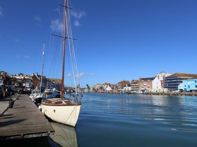 A dock with sailboats moored alongside and buildings by the water at Brewers Quay Harbour