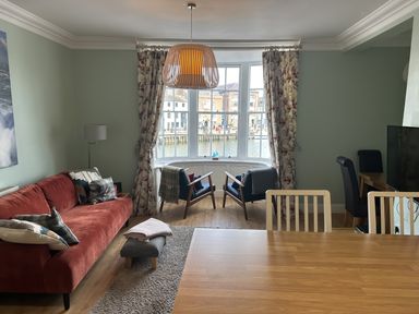 A living room with a red sofa two black armchairs a wooden dining table and a large window with floral curtains at Tradewinds Brewers Quay Harbour