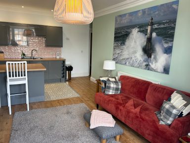 A living room with a red sofa and pillows next to a kitchen area with gray cabinets at Tradewinds Brewers Quay Harbour