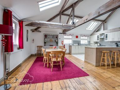 A dining area with wooden table and chairs on a red rug next to a kitchen with stools and white cabinets at Upsidedown House in Brewers Quay Harbour