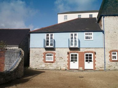 A stone and blue wooden house exterior with two white doors and windows at Upsidedown House in Brewers Quay Harbour