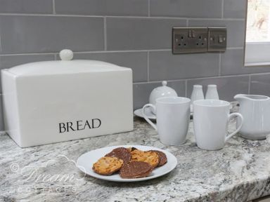 A kitchen countertop with a bread box a plate of biscuits two mugs and a jug at Upsidedown House Brewers Quay Harbour