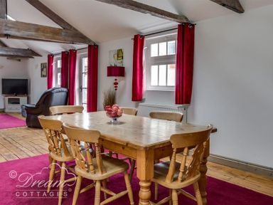 A dining area with a wooden table and six chairs with a bowl of decorative balls on the table and a living room with a black chair and television in the background at Upsidedown House Brewers Quay Harbour