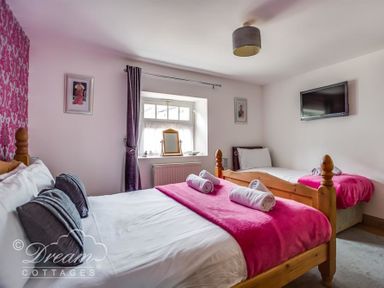 A bedroom with two beds a window with a curtain a mounted TV and framed pictures at Upsidedown House Brewers Quay Harbour