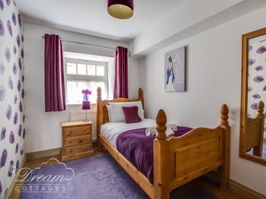 A bedroom with a wooden single bed purple bedding and curtains next to a window with a nightstand and a lamp at Upsidedown House Brewers Quay Harbour