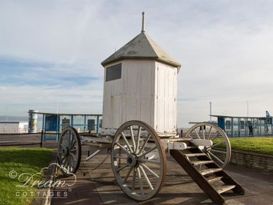 An old wooden wagon with stairs on a paved area near grassy patches and modern glass shelters at Brewers Quay Harbour