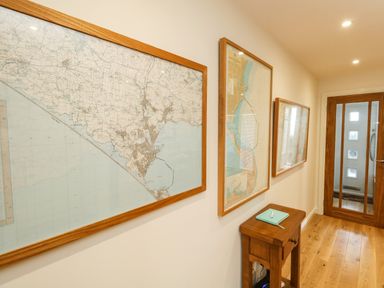 A hallway with framed maps on the wall a wooden table with a book and a wooden door at Waters Edge in Wyke Regis
