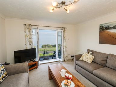 A living room with two sofas a wooden coffee table a TV and an open door leading to a balcony overlooking the sea at Waters Edge in Wyke Regis