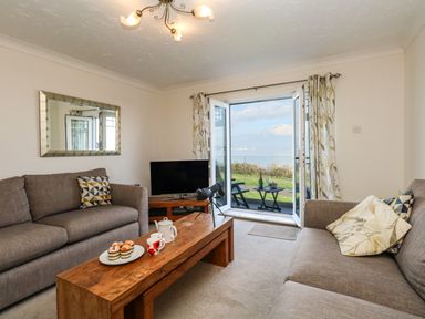 A living room with two sofas and a wooden coffee table opening to a balcony with ocean view at Waters Edge in Wyke Regis