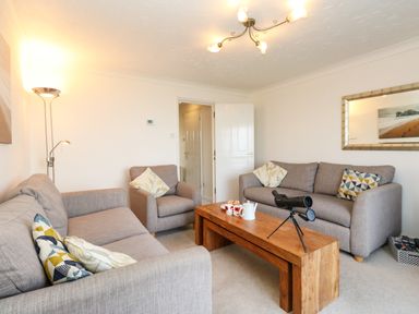 A living room with two gray sofas an armchair and a wooden coffee table with a telescope and tea set at Waters Edge in Wyke Regis