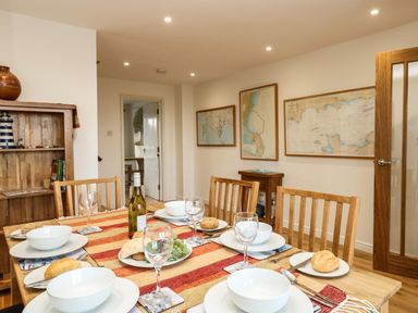A dining room with a wooden table set for six with bowls plates bread and wine with framed maps on the walls at Waters Edge in Wyke Regis