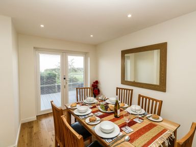 A dining room with a wooden table set for six people and a large mirror on the wall at Waters Edge in Wyke Regis