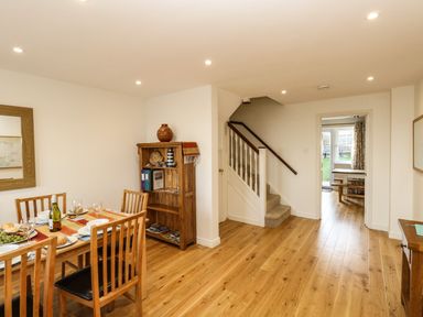 A dining area with a wooden table and chairs next to a wooden bookshelf and staircase at Waters Edge in Wyke Regis