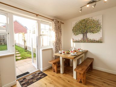A dining area with a wooden table and benches set for breakfast next to a door leading to a garden at Waters Edge Wyke Regis