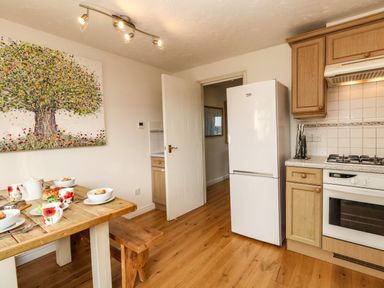 A kitchen with a wooden dining table set for breakfast a white refrigerator wooden cabinets and a stove at Waters Edge in Wyke Regis