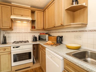 A kitchen with wooden cabinets a stove microwave kettle toaster and a sink at Waters Edge in Wyke Regis