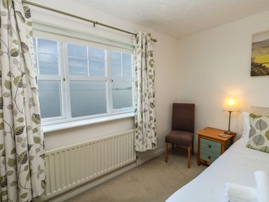 A bedroom with a window overlooking the sea a chair a bedside table with a lamp and a bed with a pillow and towel at Waters Edge in Wyke Regis