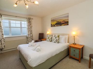 A bedroom with a double bed two bedside tables lamps and a window with patterned curtains at Waters Edge in Wyke Regis