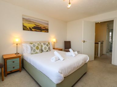 A bedroom with a double bed two bedside tables two lamps a chair and a landscape picture on the wall at Waters Edge in Wyke Regis