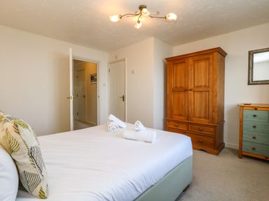 A bedroom with a bed, three rolled towels on the bed, a wooden wardrobe, a dresser with drawers, and an open door at Waters Edge Wyke Regis