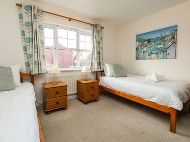 A bedroom with two single beds two wooden bedside tables with lamps a window with patterned curtains and a painting on the wall at Waters Edge Wyke Regis