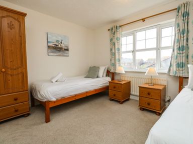 A bedroom with two single beds two bedside tables with lamps a wooden wardrobe and a window with patterned curtains at Waters Edge in Wyke Regis