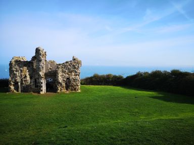 A ruined stone structure on a grassy area with a view of the sea and boats in the distance at Waters Edge in Wyke Regis