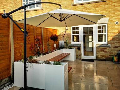 A patio with a white umbrella over built in planter benches and a door leading inside a brick house at Waters Edge in Wyke Regis
