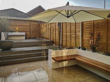 A backyard patio with tiled floor wooden steps planter with bench and umbrella at Waters Edge in Wyke Regis
