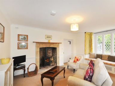 A living room with a fireplace and wood stove a sofa and armchair a coffee table a window seat with cushions and yellow curtains at Warmwell Lodge in Warmwell