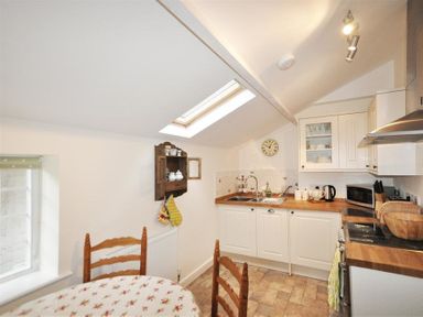 A kitchen with white cabinets wooden countertops a round table with floral tablecloth and wooden chairs at Warmwell Lodge in Warmwell