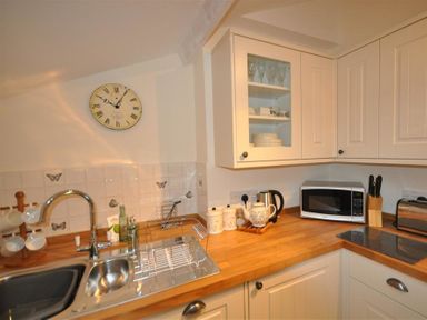 A kitchen corner with a sink, wooden countertop, white cabinets, microwave, kettle, and utensils at Warmwell Lodge in Warmwell