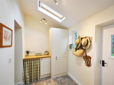 A utility room with white cabinets a wooden countertop a skylight and hats hanging on the wall at Warmwell Lodge in Warmwell