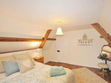 A bedroom with a bed with pillows and a blanket a bedside table with a lamp a round table with a mirror and a stool wooden beams on the ceiling at Warmwell Lodge in Warmwell