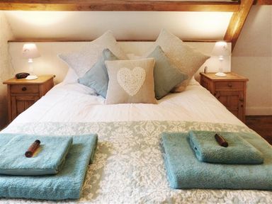 A bed with multiple pillows and folded blue towels on a patterned bedspread with two wooden nightstands and lamps at Warmwell Lodge in Warmwell