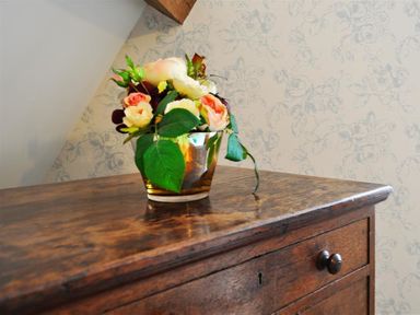 A small bouquet of flowers in a glass vase on a wooden drawer at Warmwell Lodge in Warmwell