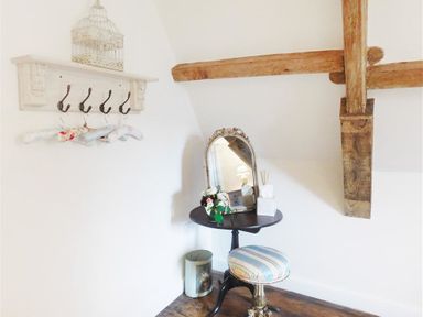 A corner with a small round table and mirror a striped stool wooden beams on the wall and a coat rack with hangers at Warmwell Lodge in Warmwell