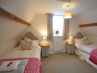 A bedroom with two single beds side by side with nightstands and lamps under a window at Warmwell Lodge in Warmwell