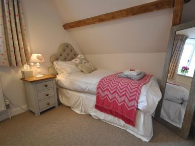 A bedroom with a single bed a bedside table with a lamp a framed mirror and floral curtains at Warmwell Lodge in Warmwell