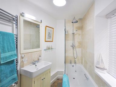 A bathroom with a bathtub shower combination a sink with cabinet a mirror towel rack with blue towels and a window with blinds at Warmwell Lodge in Warmwell