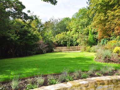 A garden with a green lawn surrounded by trees shrubs and flowers at Warmwell Lodge in Warmwell