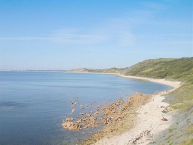 A coastal scene with a rocky beach and hills covered with vegetation at Warmwell Lodge in Warmwell
