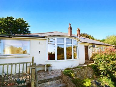 A white single-story house with a curved window and two chimneys surrounded by greenery at Waterson in Osmington