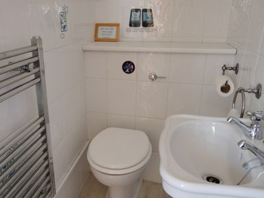 A small bathroom with a toilet, sink, towel rack, toilet paper holder, and signs on the tiled wall at Waterson in Osmington
