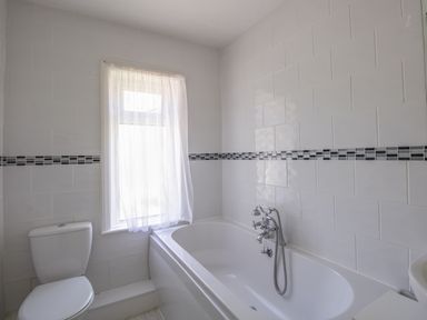 A bathroom with a bathtub and toilet near a window with a sheer curtain at Waterson in Osmington