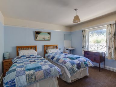 A bedroom with two single beds with patchwork quilts a window with curtains a wooden chest and a washbasin at Waterson in Osmington