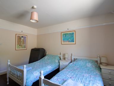 A bedroom with two single beds with blue floral bedding two bedside tables with lamps and framed paintings on walls at Waterson in Osmington